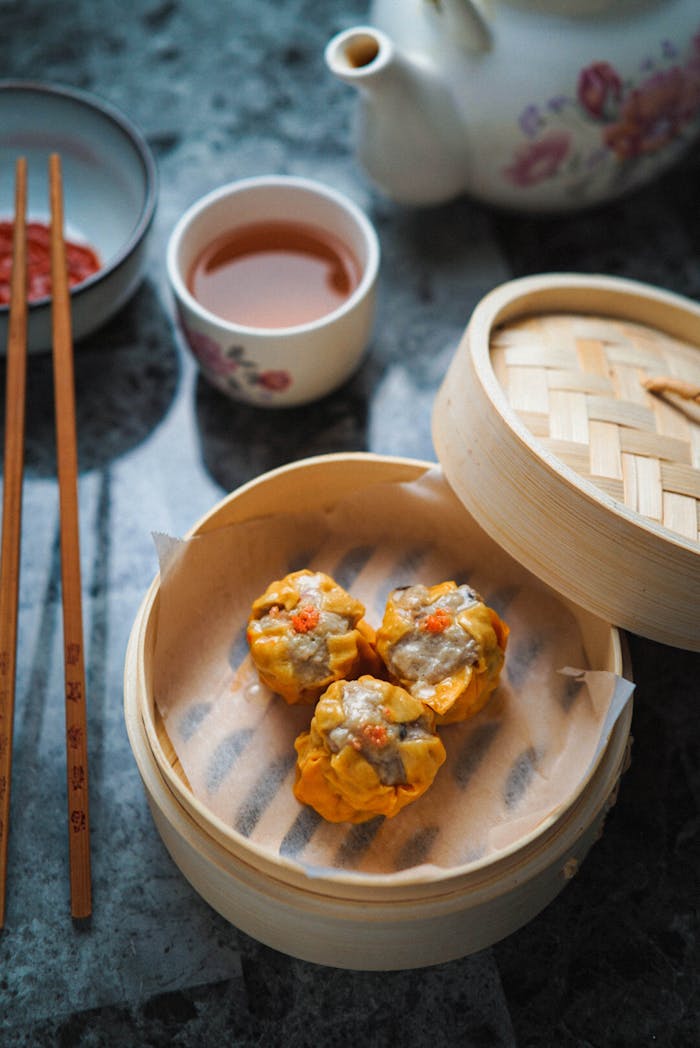 Close-up of dim sum served in a bamboo steamer with tea, chopsticks, and traditional table setting.